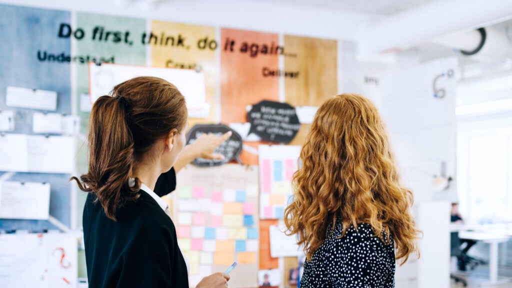 Two women looking at a white board