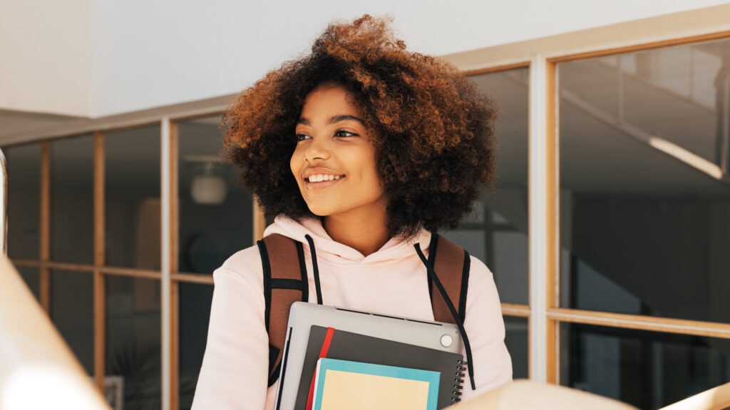 A young girl holding a laptop and books.