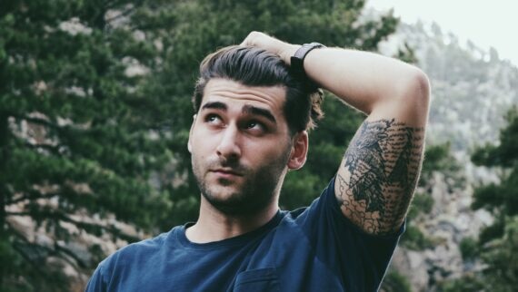 Man with tattooed upper arm looks thoughtfully into the distance.