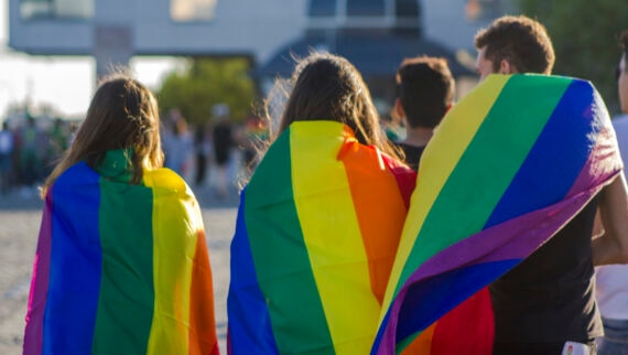 Showing 3 people from the back wearing the LGBTQIA+ flag