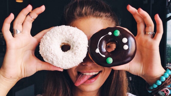 Woman holding to doughnuts in front of her face and sticking her tongue out in a playful way.