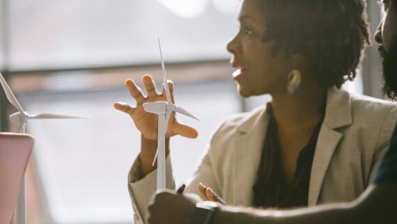 A woman in a professional setting discussing a model of a wind turbine, illustrating a focus on renewable energy or engineering.