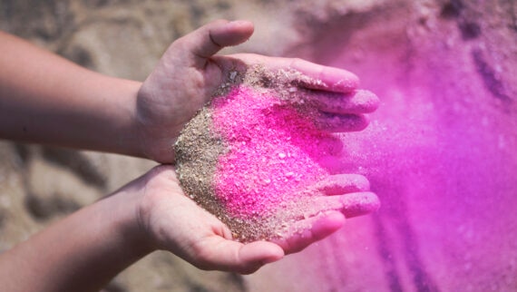 Close-up of hands holding purple sand in the shape of a heart.