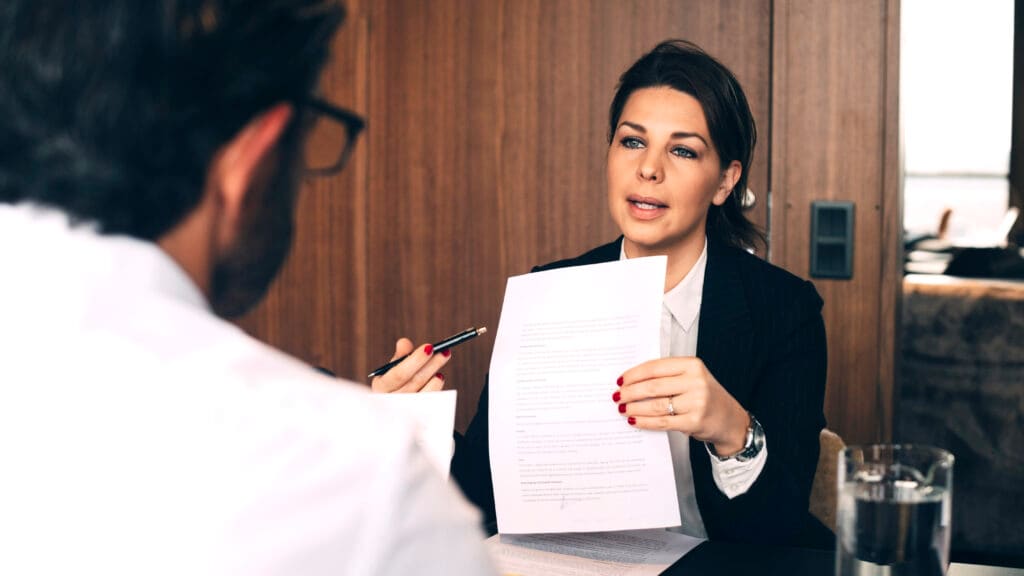 A woman holding up a CV whilst she is talking to a man in a meeting.