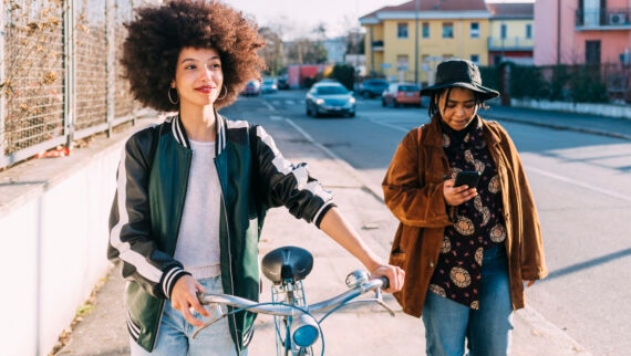 Young woman carrying bicycle with female friend