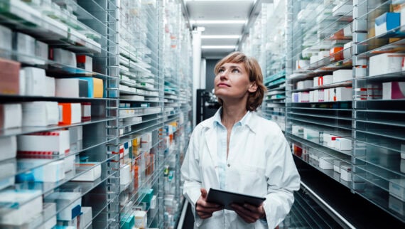 Female pharmacist looking at medicine while holding digital tablet at pharmacy stock room.