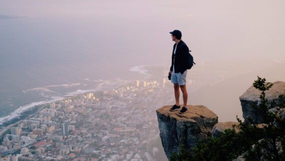 Young man standing on a rock looking over a city to the sea.