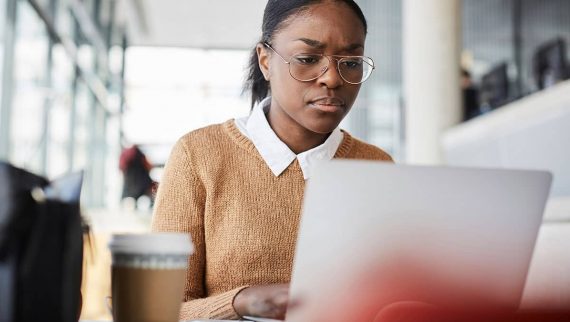 A black woman wearing glasses working on her laptop in the office.