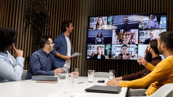 A boardroom meeting with a combo of workers in the office and working remotely