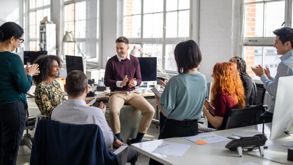 A group of workers applauding one of their colleagues in an office environment