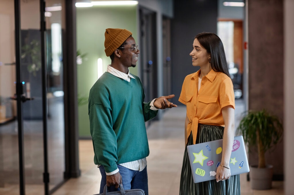 Two young professionals having a casual conversation in a modern office, showcasing a positive workplace culture designed to attract young talent.