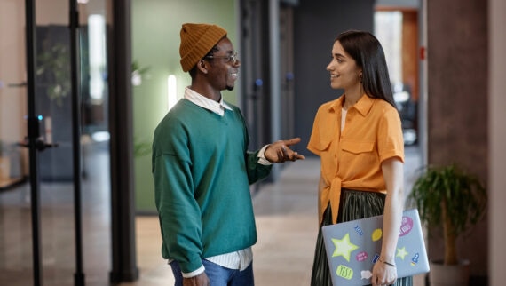 Two young professionals having a casual conversation in a modern office, showcasing a positive workplace culture designed to attract young talent.