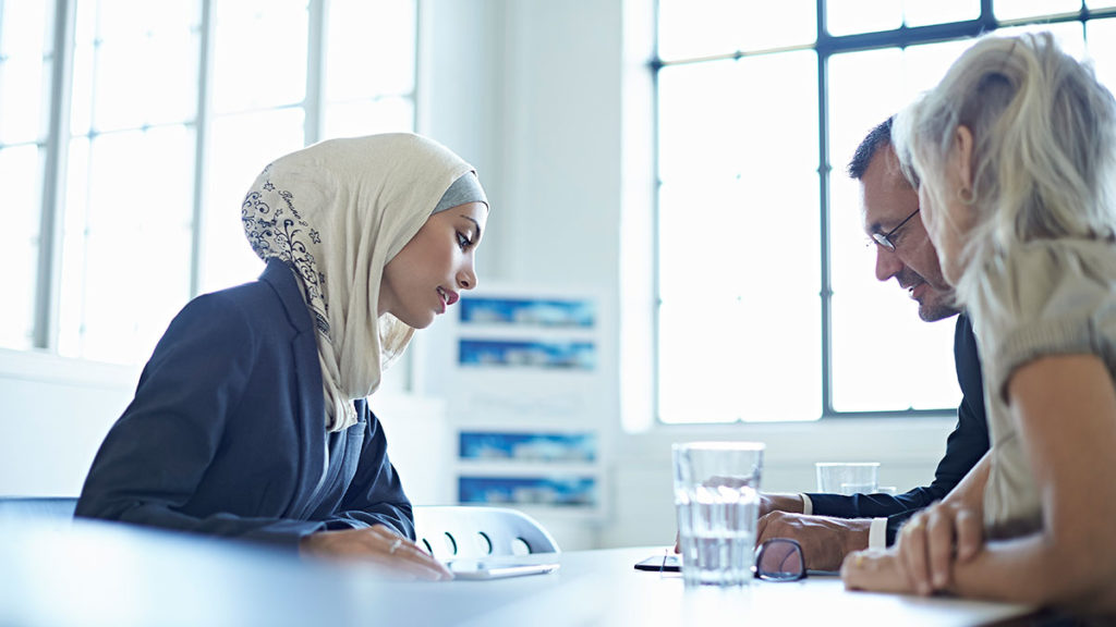 An image of a man and a woman looking at documents as they interview a woman for a job.