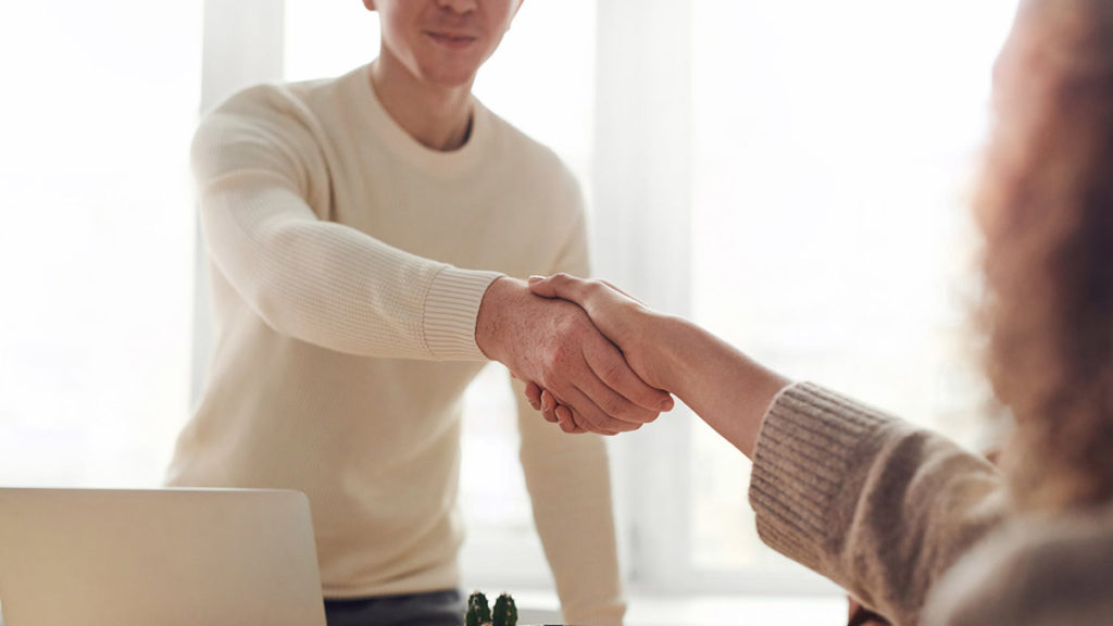 An image of a man and woman shaking hands as they greet each other at a job interview. 