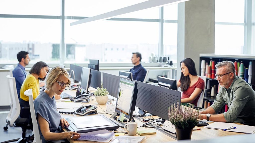 An image showing a group of people working at their desks in an office.