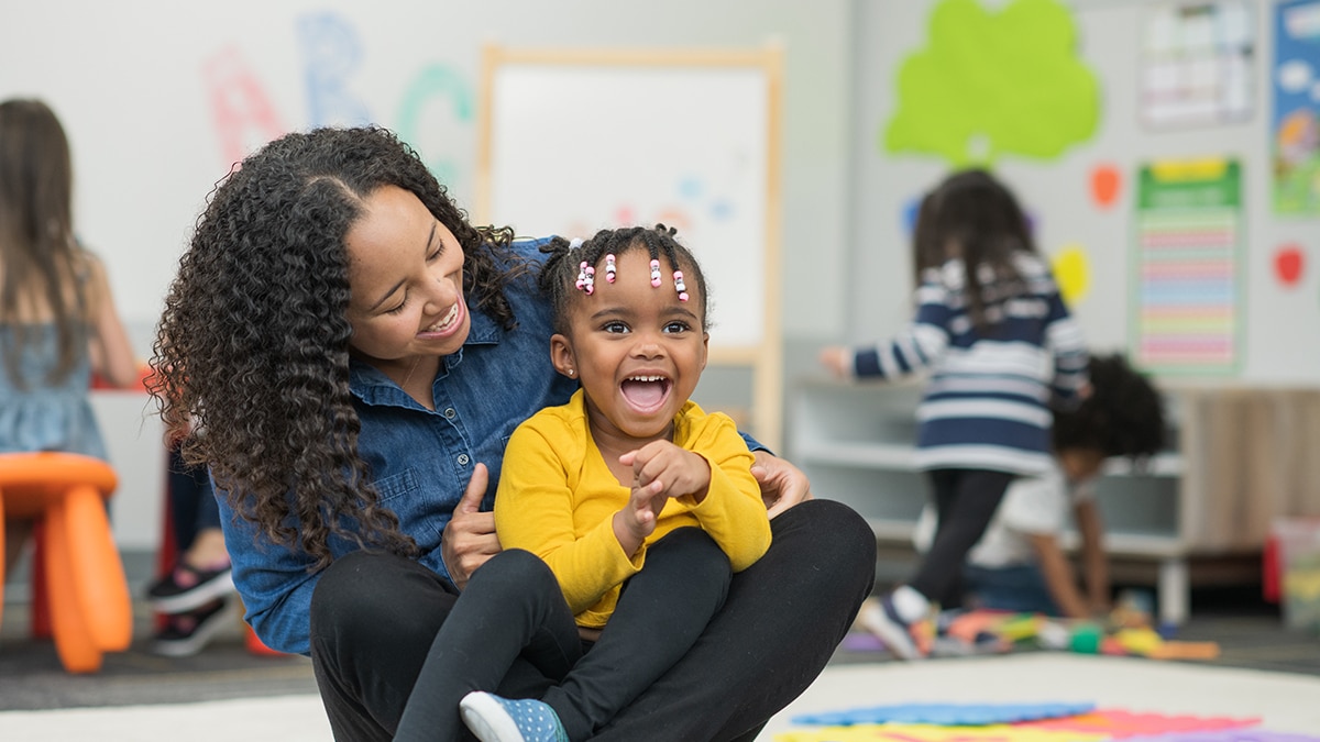 Happy young girl sitting on teachers lap