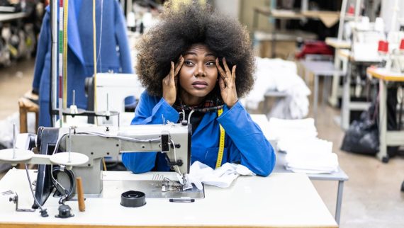 An image of an employee working with a sewing machine, looking stressed.