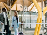 business couple of coworkers walking with luggage at the airport talking and looking at each other