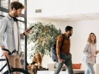 Young business man arriving to the office with his bike. He is using his phone, suggesting a cycle to work scheme as part of a wider employee benefits package
