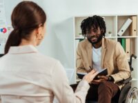 A young black man on a wheelchair discussing something with colleague in the office