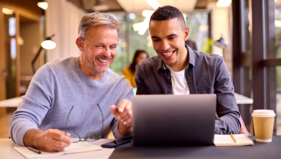 a younger and older colleague working together on a project, viewing something on the laptop screen