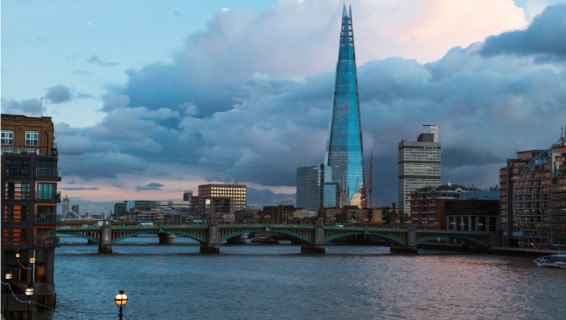 Aerial view of the London skyline at dusk, with the Shard rising above the Thames and Southwark Bridge, under a dramatic cloudy sky.
