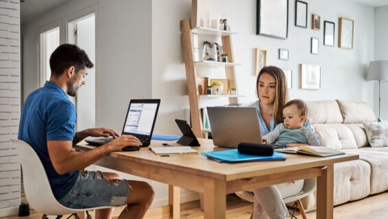Young man and woman with baby sitting at table and using laptops while working on remote project at home