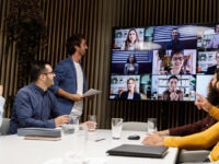 A boardroom meeting with a combo of workers in the office and working remotely