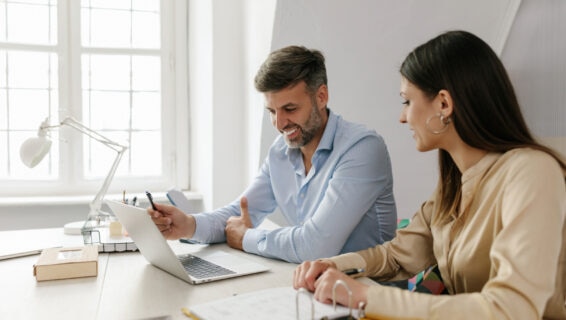 Two businesspeople talking in an office environment, working together on or viewing a new report