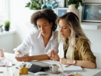 Portrait of two elegant women sitting in a home office and working together on a project