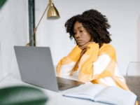 Young professional woman showing signs of fatigue while working on a laptop, illustrating the importance of employee burnout prevention and mental health awareness in the workplace.