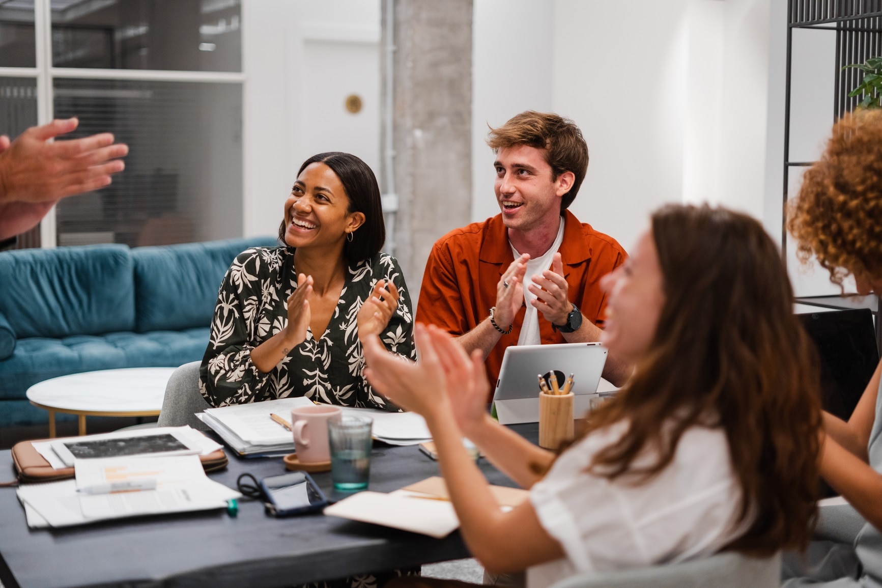 Group of diverse colleagues sitting at table and applauding excited with great news and business achievements while having meeting in modern coworking space.