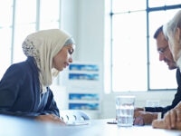 An image of a man and a woman looking at documents as they interview a woman for a job.