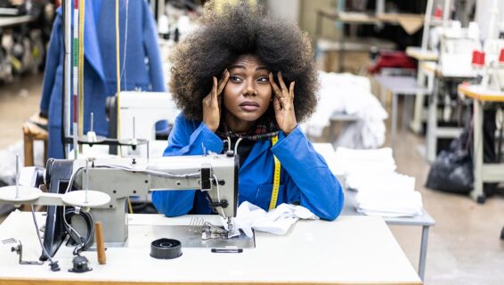 An image of an employee working with a sewing machine, looking stressed.