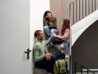 Happy, laughing and talking young coworker friends sitting on stairs of office building entering office of modern startup small business, showing the value of workplace friendships